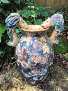 Multicolored vase with 2 lions as handles in a garden.